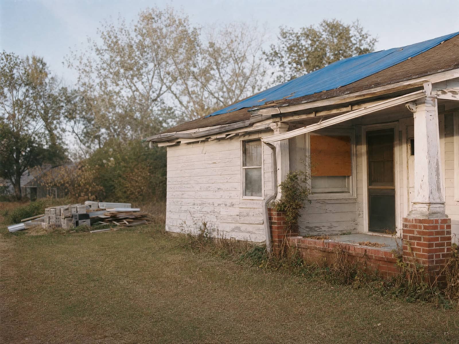 A worn older Hampton Roads house showing decades of deferred repairs, warm late light.