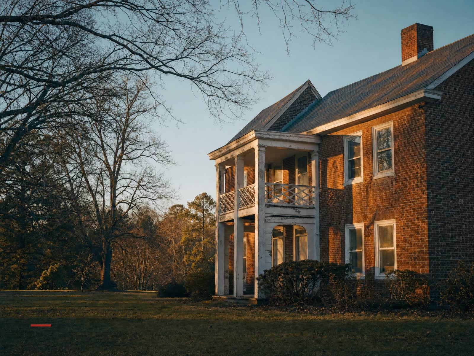 An older brick colonial with age and character, empty and quiet in golden-hour light.